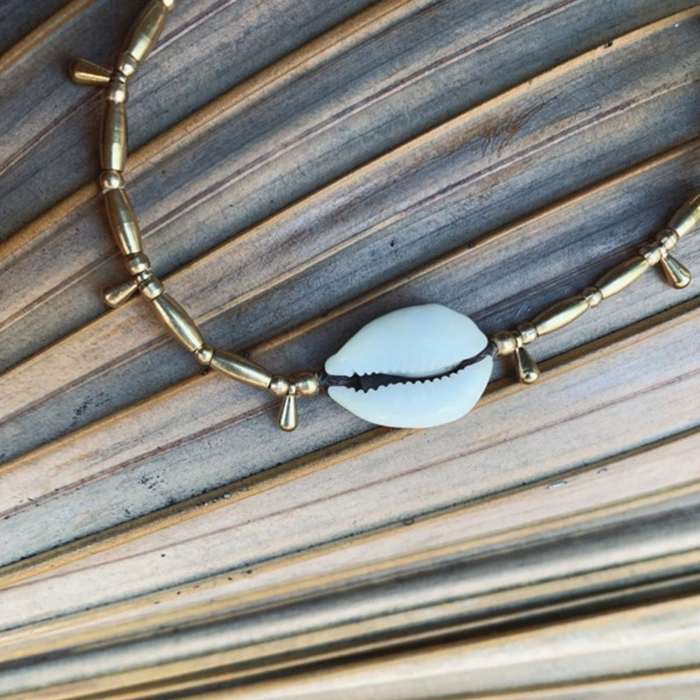 Close up detail of adjustable cowrie shell anklet showing brass droplets and sliding knot