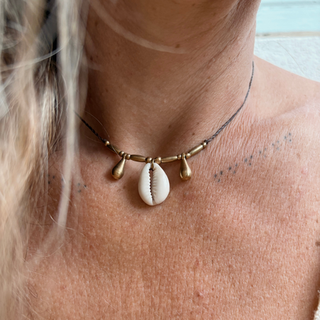 Close-up of cowrie and brass teardrop necklace showing natural shell detail and artisan metalwork, coastal minimalist design